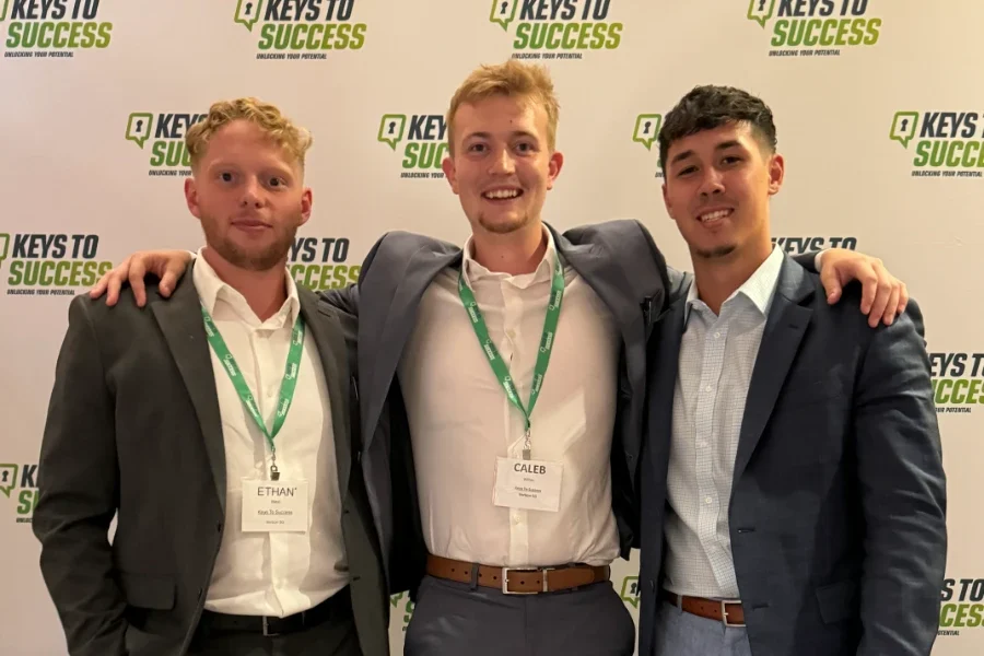 Three young men posing together at a "Keys to Success" event backdrop.