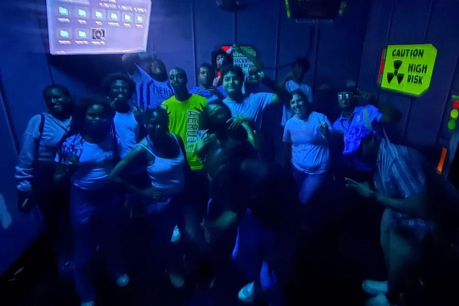 Group of people posing together in a dimly lit room with neon accents and caution signs.